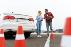 Une élève et son moniteur devant une voiture blanche, entre des plots orange